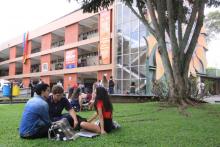 Fotografía de las zonas cercanas a la Biblioteca Rodrigo Facio, de la Universidad de Costa Rica. Estudiantes acostados en el césped y hablando, otros estudiantes caminan por el lugar.