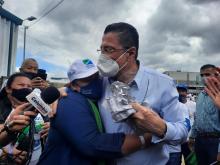 Fotografía del candidato presidencial Rodrigo Chaves, con mascarilla, siendo abrazado por una mujer con una gorra y mascarilla de su partido.